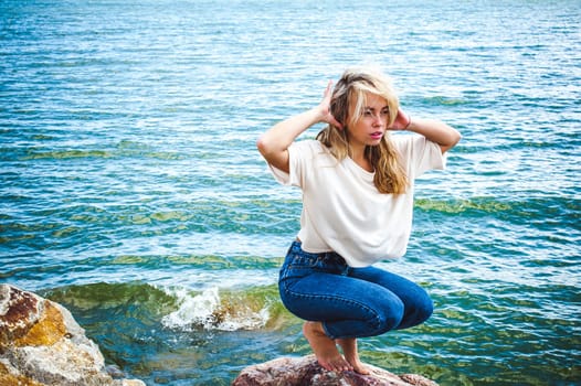 Portrait young woman on stones near sea. Beautiful girl is resting on coast, enjoying outdoor recreation.