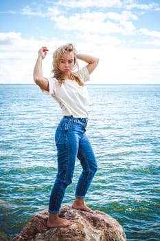 Portrait young woman on stones near sea. Beautiful girl is resting on coast, enjoying outdoor recreation.