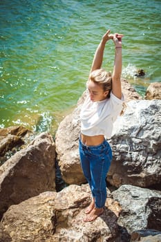Portrait young woman on stones near sea. Beautiful girl is resting on coast, enjoying outdoor recreation.