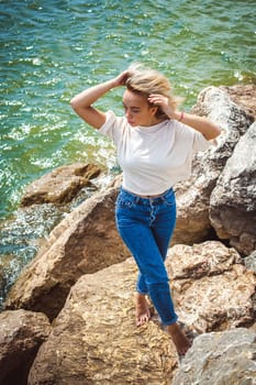 Portrait young woman on stones near sea. Beautiful girl is resting on coast, enjoying outdoor recreation.