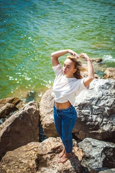 Portrait young woman on stones near sea. Beautiful girl is resting on coast, enjoying outdoor recreation.