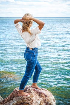 Portrait young woman on stones near sea. Beautiful girl is resting on coast, enjoying outdoor recreation.