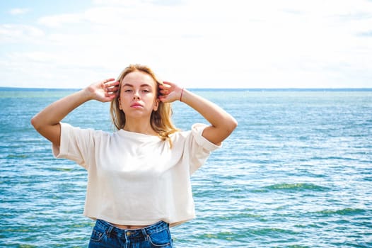 Portrait young woman on stones near sea. Beautiful girl is resting on coast, enjoying outdoor recreation.