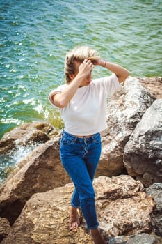 Portrait young woman on stones near sea. Beautiful girl is resting on coast, enjoying outdoor recreation.