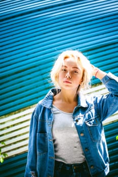 young woman in jeans clothes outdoors. portrait of a girl with freckles on her face, against the background of a metal striped fence, on a sunny summer day
