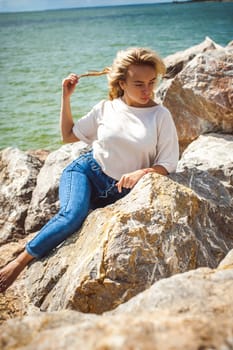 Portrait young woman on stones near sea. Beautiful girl is resting on coast, enjoying outdoor recreation.