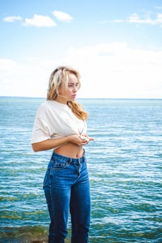Portrait young woman on stones near sea. Beautiful girl is resting on coast, enjoying outdoor recreation.