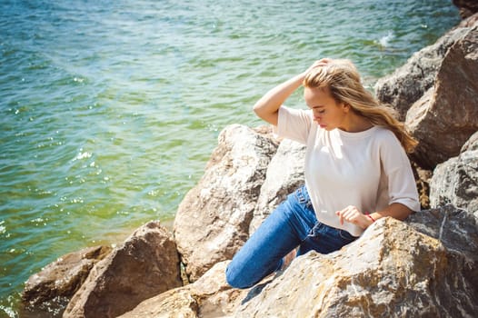 Portrait young woman on stones near sea. Beautiful girl is resting on coast, enjoying outdoor recreation.