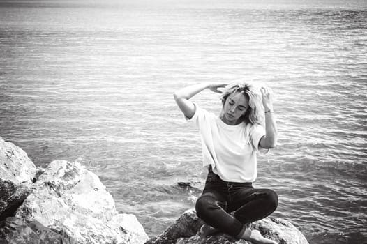 Portrait young woman on stones near sea. Beautiful girl is resting on coast, enjoying outdoor recreation.