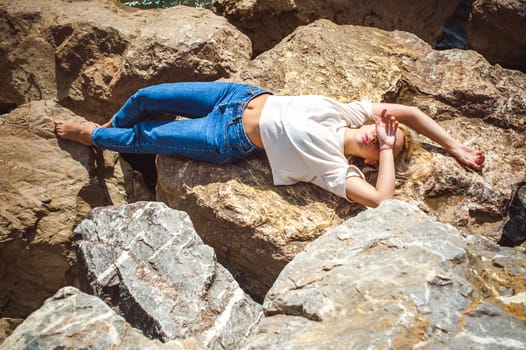 Portrait young woman on stones near sea. Beautiful girl is resting on coast, enjoying outdoor recreation.