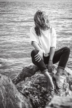 Portrait young woman on stones near sea. Beautiful girl is resting on coast, enjoying outdoor recreation.