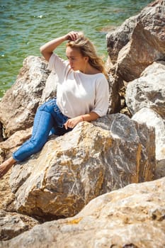 Portrait young woman on stones near sea. Beautiful girl is resting on coast, enjoying outdoor recreation.