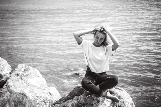 Portrait young woman on stones near sea. Beautiful girl is resting on coast, enjoying outdoor recreation.