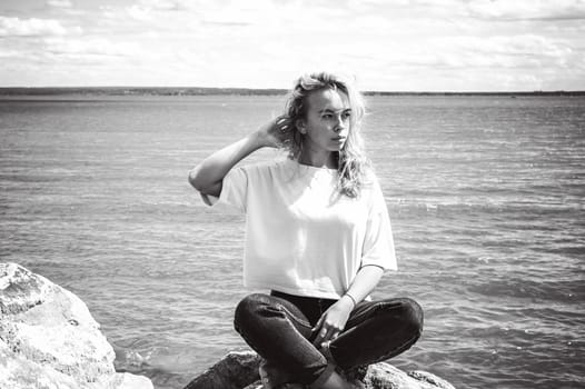 Portrait young woman on stones near sea. Beautiful girl is resting on coast, enjoying outdoor recreation.