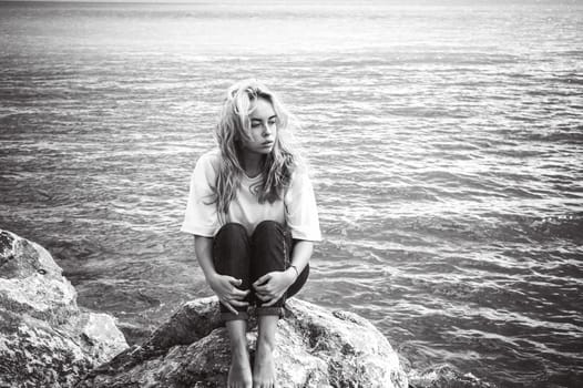 Portrait young woman on stones near sea. Beautiful girl is resting on coast, enjoying outdoor recreation.