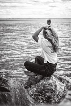 Portrait young woman on stones near sea. Beautiful girl is resting on coast, enjoying outdoor recreation.