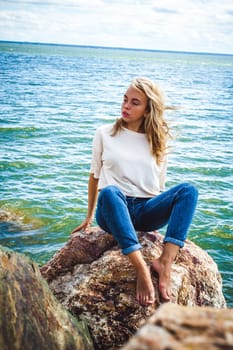 Portrait young woman on stones near sea. Beautiful girl is resting on coast, enjoying outdoor recreation.