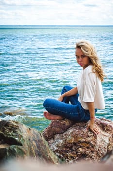 Portrait young woman on stones near sea. Beautiful girl is resting on coast, enjoying outdoor recreation.