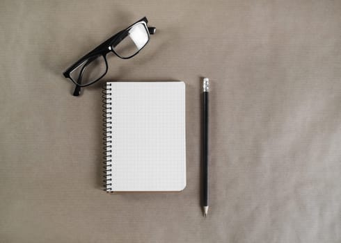 Blank notepad, glasses and pencil on craft paper background. Flat lay.
