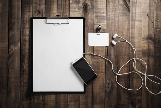 Blank paperwork template. Responsive design mockup. Clipboard, letterhead, smartphone, badge and headphones on wood table background. Flat lay.