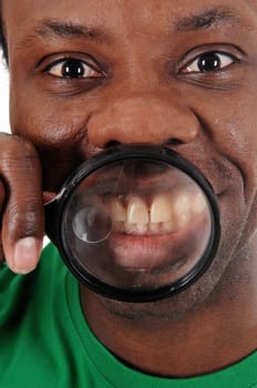 African American man holding a magnifying glass over his teeth's.in a closeup image, with big eyes.