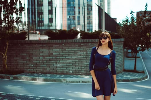 Young attractive woman with long legs with long hair in a blue elegant dress with a sword belt, strolls in a European modern courtyard, a warm summer day