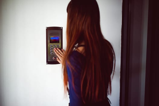attractive woman in a blue elegant dress, dials code into intercom, at entrance of house