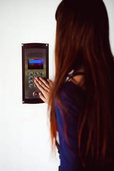 attractive woman in a blue elegant dress, dials code into intercom, at entrance of house