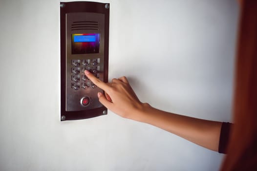 attractive woman in a blue elegant dress, dials code into intercom, at entrance of house