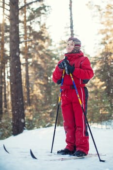 A little boy in red clothes is skiing in a pine forest