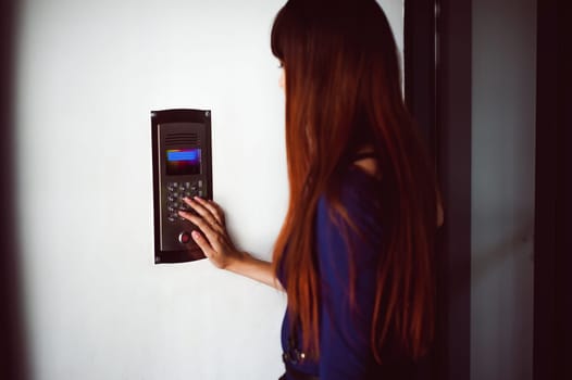 attractive woman in a blue elegant dress, dials code into intercom, at entrance of house