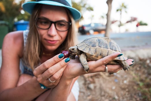 Happy young woman feeding turtle with cherry