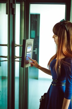 attractive woman in a blue elegant dress, dials code into intercom, at entrance of house