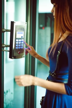 attractive woman in a blue elegant dress, dials code into intercom, at entrance of house