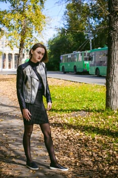 street portrait of a girl student, fashionably dressed in dark clothes, with a black backpack and denim jacket autumn sunny day