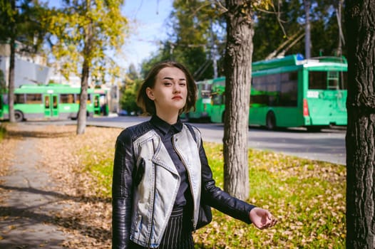street portrait of a girl student, fashionably dressed in dark clothes, with a black backpack and denim jacket autumn sunny day