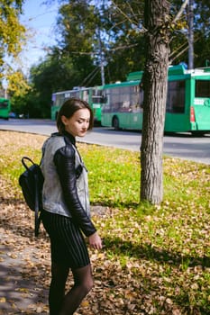 street portrait of a girl student, fashionably dressed in dark clothes, with a black backpack and denim jacket autumn sunny day
