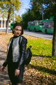 street portrait of a girl student, fashionably dressed in dark clothes, with a black backpack and denim jacket autumn sunny day