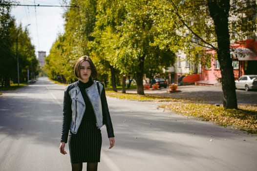 street portrait of a girl student, fashionably dressed in dark clothes, with a black backpack and denim jacket autumn sunny day