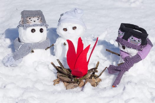 Cute little snowmen dressed for winter, huddled around a fire trying to keep warm. Snow covered scene in Norfolk UK