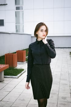 street portrait of a student girl dressed fashionably in dark clothes, on an autumn sunny day