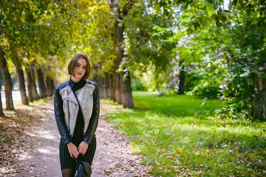 street portrait of a girl student, fashionably dressed in dark clothes, with a black backpack and denim jacket autumn sunny day