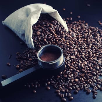 Still life with roasted coffee beans, canvas bag and holder from espresso machine.