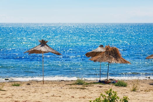 Straw beach umbrellas. Straw parasols. Sunny day on the beach.