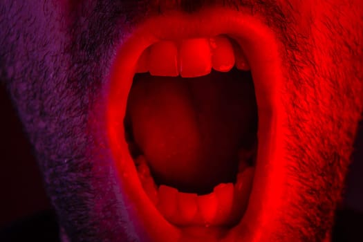 Macro closeup on man shouting with mouth wide open. Portrait with angry facial expression.