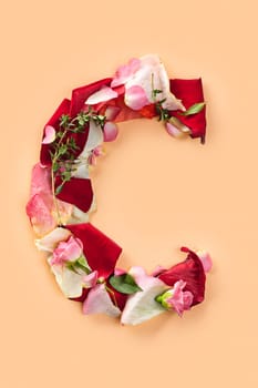 Letter C made from red roses and petals isolated on a beige background