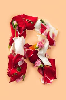 Letter R made from red roses and petals isolated on a beige background