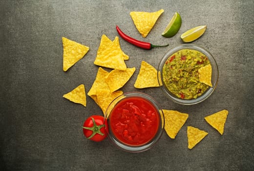 Avocado guacamole and tomato salsa with fresh ingredients on table