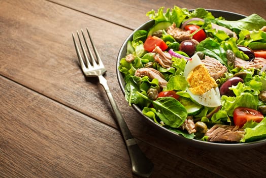 Tuna salad with lettuce, tomatoes and olives on wooden table