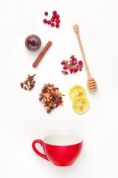 Beautiful and delicious dried tea leaves with herbs, flowers, berries, fruits falling in cup of tea over white background